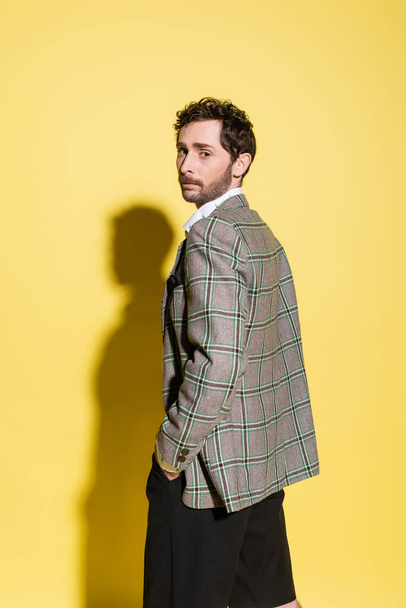 Trendy man in checkered jacket looking at camera on yellow background  - Foto, Imagen