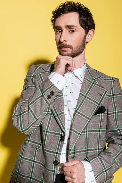 Portrait of trendy man in checkered jacket looking at camera on yellow background  - Foto, Imagem