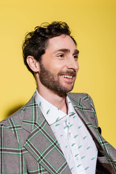 Portrait of smiling bearded man in shirt and jacket looking away on yellow background  - Foto, Bild