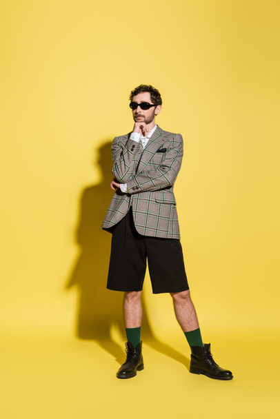 Charming guy in sunglasses and jacket posing on yellow background  - Foto, Bild