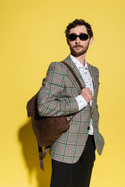 Trendy model in sunglasses posing with backpack on yellow background  - Φωτογραφία, εικόνα