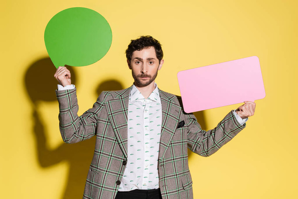 Charming guy in jacket holding speech bubbles on yellow background  - Photo, Image