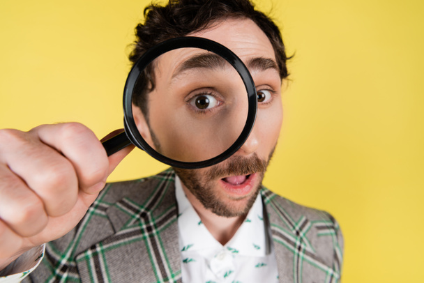 Wide angle view of stylish man looking through magnifying glass isolated on yellow   - Photo, Image