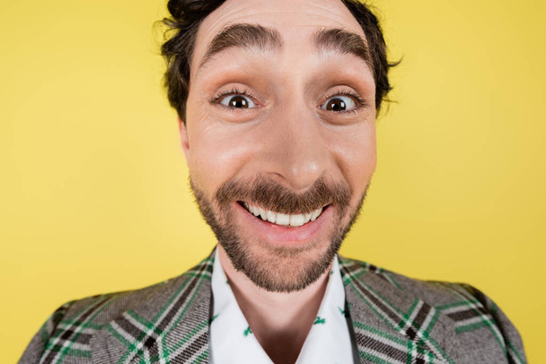 Широкий кут зору веселого чоловіка в плетеній куртці, який дивиться на камеру ізольовано на жовтому
   - Фото, зображення