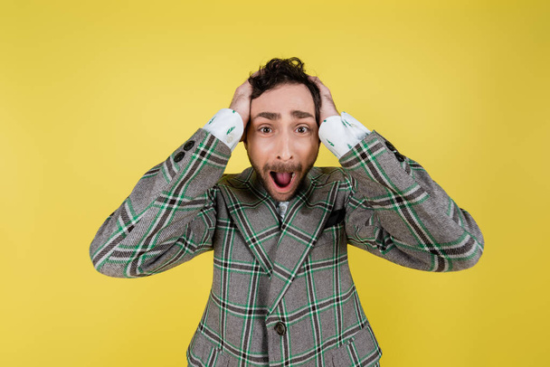 Ουρλιάζοντας άντρας με μπουφάν που καλύπτει αυτιά απομονωμένα στο κίτρινο   - Φωτογραφία, εικόνα