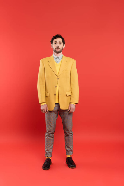 Full length of trendy model in yellow jacket standing on red background - Фото, зображення