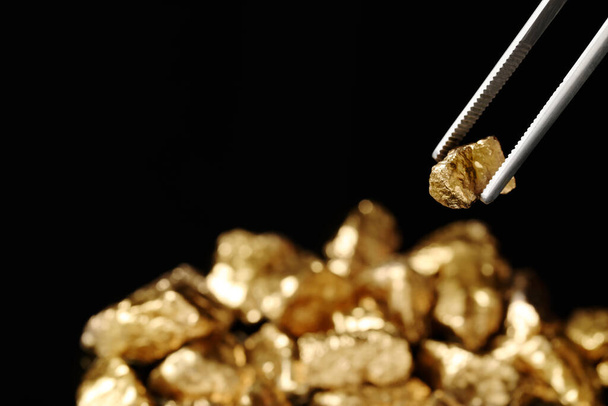 Tweezers with gold nugget against blurred background, closeup. Space for text - Foto, Imagen