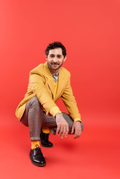 Cheerful trendy model looking at camera while posing on red background - Φωτογραφία, εικόνα