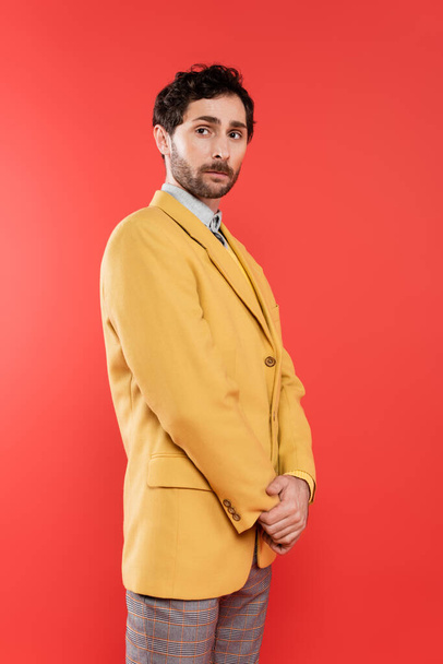 Stylish charming guy in yellow jacket standing on coral red background  - Fotoğraf, Görsel