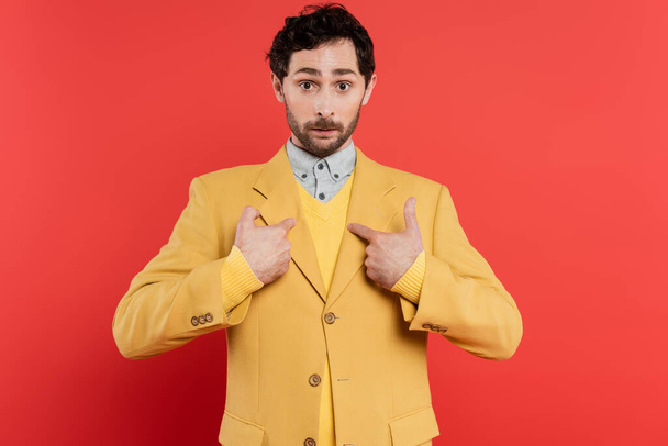 Surprised and stylish man pointing with fingers at himself on coral red background  - 写真・画像