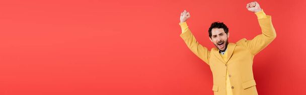 excited man with opened mouth gesturing while looking at camera on coral background, banner  - 写真・画像