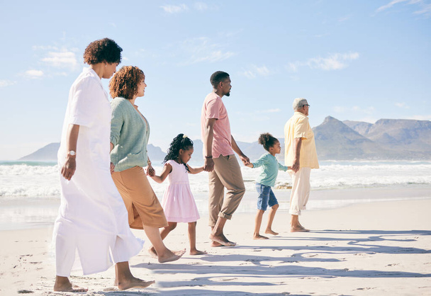 家族はビーチを歩き、旅行し、世代、団結、愛との自由と手を携えて、一緒に屋外にいます。祖父母、両親、子供、熱帯の目的地を持つ休日の人々. - 写真・画像