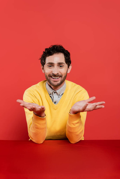 carefree man in yellow long sleeve jumper gesturing on red coral background  - Fotografie, Obrázek