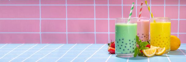 Set of three colorful summer bubble tea, bright creamy pearl tea or latte tapioca drinks, pink berry, yellow citrus, green mint, with tapioca balls and crushed ice, on colorful tile background - Photo, Image