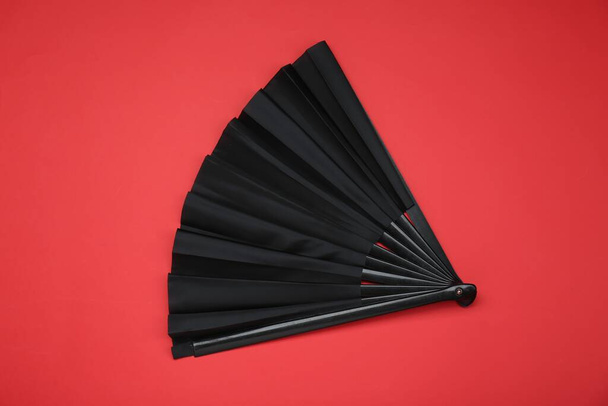 Stylish black hand fan on red background, top view - Foto, Imagen