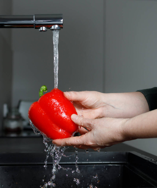 Friss piros paprika a víz alatt patak mosogató, nő a konyhában mosás zöldségek főzés előtt, nincs arc - Fotó, kép