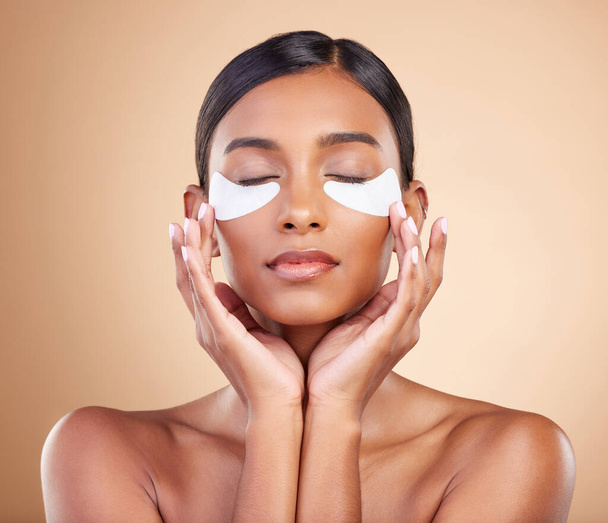 Face, beauty or Indian woman with eye patch for skincare or wellness isolated on studio background. Cosmetics or girl model with facial collagen pads or dermatology product for anti aging or glow. - 写真・画像