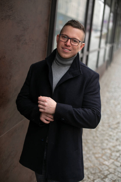 Handsome smiling man in glasses and black coat near building. Portrait of happy business man walking outdoors in cold day. Elegant middle aged person. Casual male outwear, stylish street style. - Photo, Image