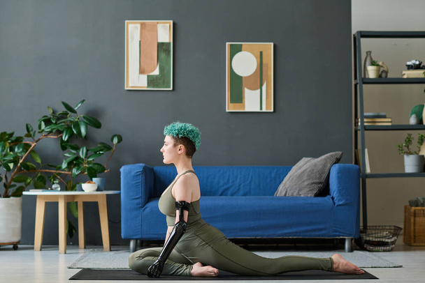 Mladá žena se zdravotním postižením dělá strečink cvičení na cvičení podložka v obývacím pokoji doma - Fotografie, Obrázek