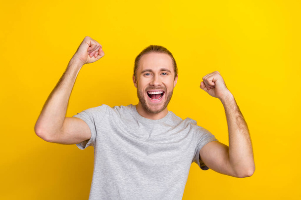 Portrait of optimistic good mood guy with long hair dressed light t-shirt raising fists win betting isolated on yellow color background. - Fotografie, Obrázek
