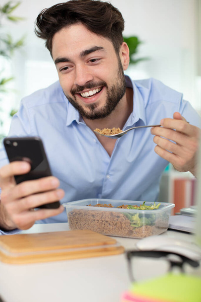 man eating breakfast whilst checking mobile phone - Φωτογραφία, εικόνα