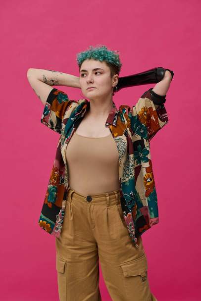 Portrait of young woman with prosthetic arm in stylish clothing posing against pink background - Photo, Image