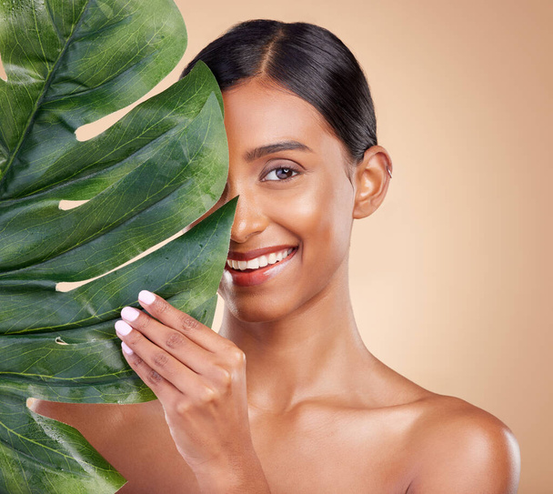 Portrait, facial and palm leaf with a model woman in studio on a beige background for natural skincare. Beauty, face and nature with an attractive young female posing for cosmetics or luxury wellness. - Foto, afbeelding