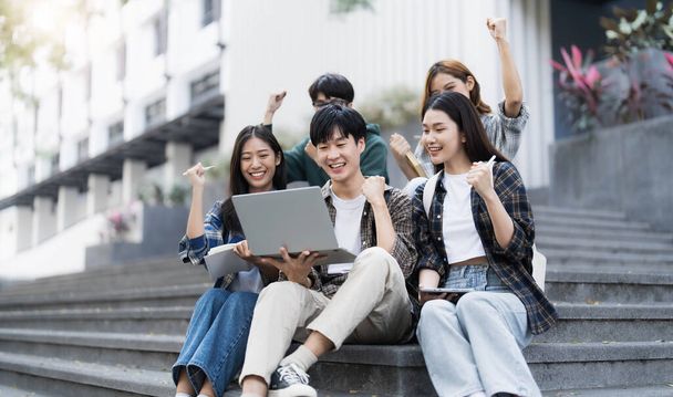 Skupina veselých asijských vysokoškoláků sedících na schodech, ukazujících pěsti, oslavujících triumf.. - Fotografie, Obrázek