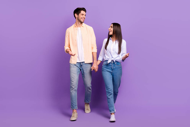 Full length portrait of two idyllic positive people hold hands walking chatting speak isolated on purple color background. - Φωτογραφία, εικόνα