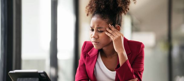 Africká americká podnikatelka v obleku čtení účetní informace o novém podnikání na digitálním tabletu se stresující a bolesti hlavy při práci a myšlení strategie projektu v moderním pracovním prostoru. - Fotografie, Obrázek