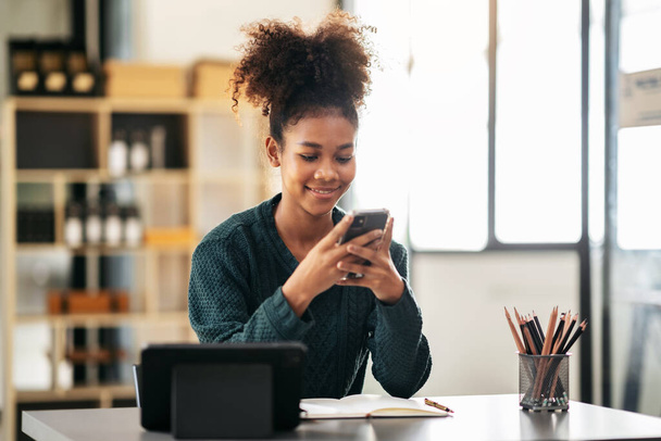Estudiante afroamericana en suéter usando smartphone después de ver e-learning y estudiar lección en línea en tableta mientras se sienta a aprender conocimiento y educación en la universidad. - Foto, imagen