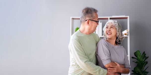 Senior couple hugging with love while drinking coffee and spending time to doing activity for relaxation in life retirement together at living room of home. - Фото, зображення