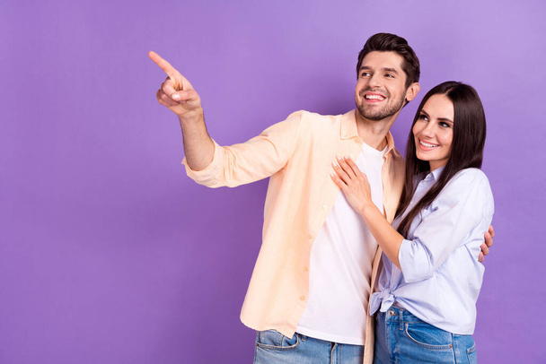Photo of cheerful optimistic couple lovely people cuddles man directing finger empty space romantic tv show isolated on purple color background. - Foto, Imagen