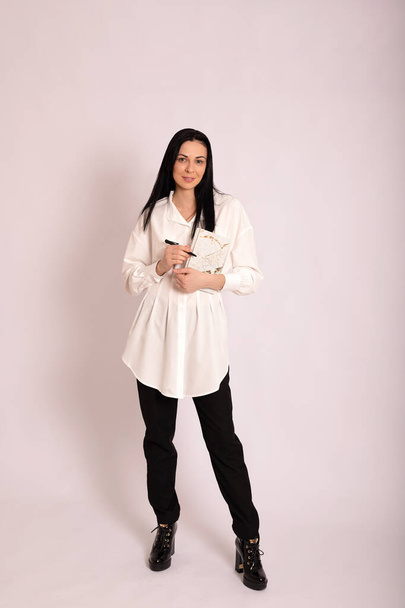 Mladá žena s poznámkovým blokem a perem v rukou v klasických šatech na bílém pozadí. Kvalitní fotografie - Fotografie, Obrázek
