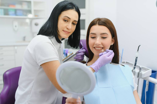 Young woman choosing color of teeth at dentist. - Foto, afbeelding