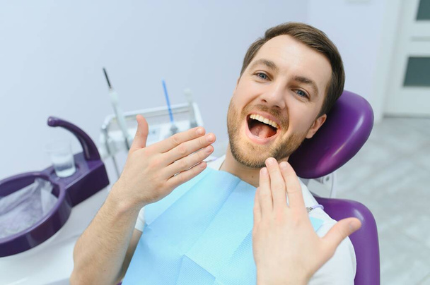 Handsome man smiling while teeth exam. Happy male patient sitting in a dentist's chair and having check up teeth - Foto, Imagem