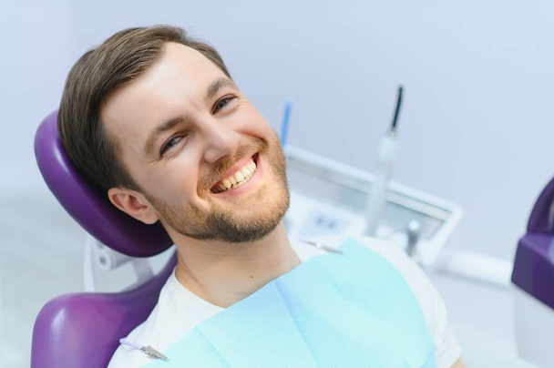 Handsome man smiling while teeth exam. Happy male patient sitting in a dentist's chair and having check up teeth - Φωτογραφία, εικόνα