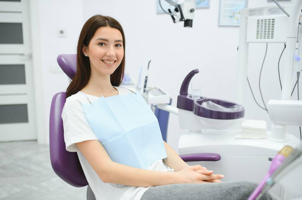 The girl is at the reception at the dentist. A happy client at the dentist smiles. . Dental bleaching. Dental clinic. Treatment of teeth in a modern clinic. Restoration of a healthy smile. Successful. - Фото, изображение