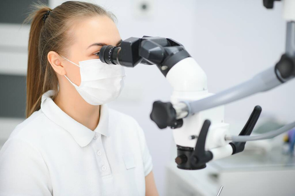 Female dentist using dental microscope treating patient teeth at dental clinic office. - Photo, Image