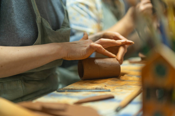 Cerca de manos humanas haciendo una taza de barro. Clase de enseñanza de cerámica. Potter hace platos de arcilla, cerámica. Artesanía, trabajo a mano en el taller. - Foto, imagen