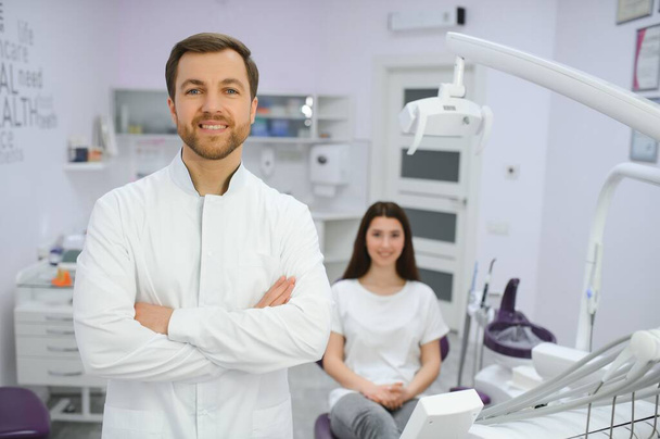 Portrait of positive male dentist with crossed hands posing at camera with patient and nurse on background. - Фото, зображення