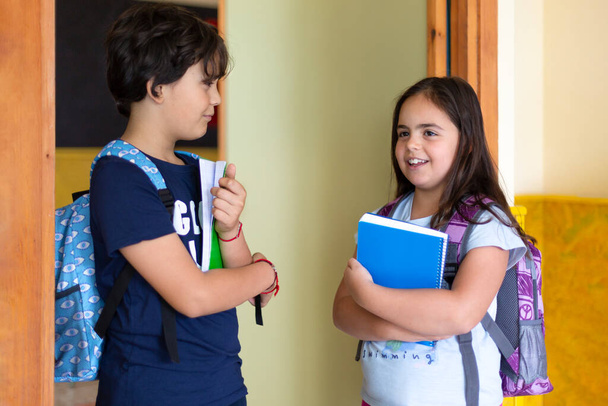 Мальчик разговаривает с девушкой за пределами класса. Счастливого кавказского младшего школьного возраста. Молодые ученики общаются. - Фото, изображение