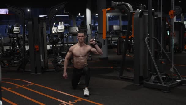 muscular sportsman squatting in sport gym with kettlebell. sportsman squatting with kettlebell in gym. sportsman with sport kettlebell equipment in gym - Footage, Video