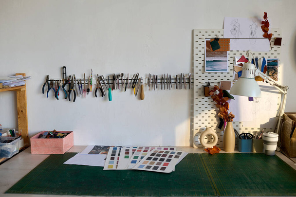 Part of workshop of tanner with sample swatches, box with leather pieces and other supplies on table and row of handtools on the wall - Foto, Bild