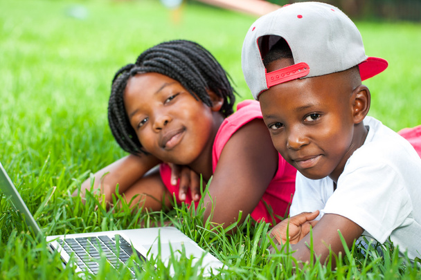 Afrykańskie dzieci na trawie z laptopa. - Zdjęcie, obraz