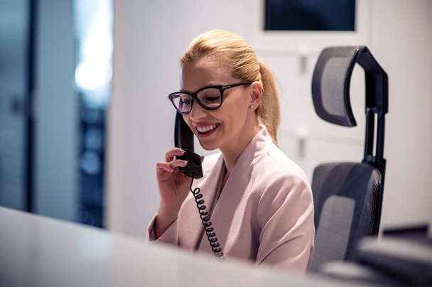 Бізнес-леді розмовляє по телефону з посмішкою, сидячи на робочому місці
. - Фото, зображення
