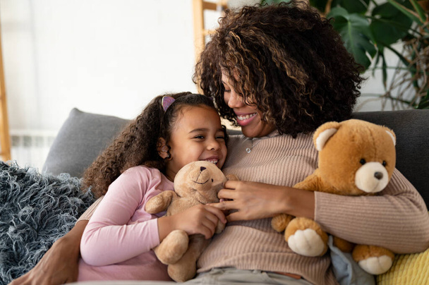 afro-amerikai anya és lánya otthon ölelkeznek a kanapén - Fotó, kép