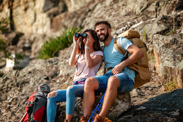 Young couple of hikers having a rest on mountains, looking through binoculars.Travel, hobbies and hiking concept - Photo, Image