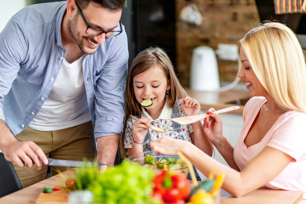 Moeder, vader en dochter snijden groente. Mensen, voedsel, geluk en levensstijl concept. - Foto, afbeelding