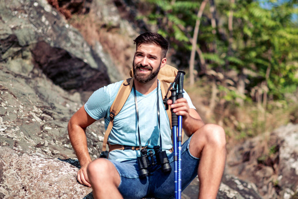 Mladý pohledný muž turistika přes hory s turistickými holemi. - Fotografie, Obrázek
